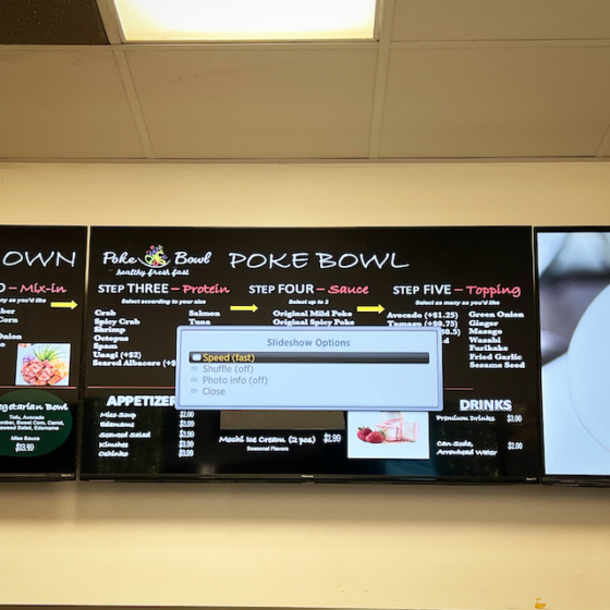 This is a photo of a large TV screen in the mall food court showing the menu for poke. On top of there menu for poke is the computer's equivalent of a menu:  a list of "slideshow options" 
